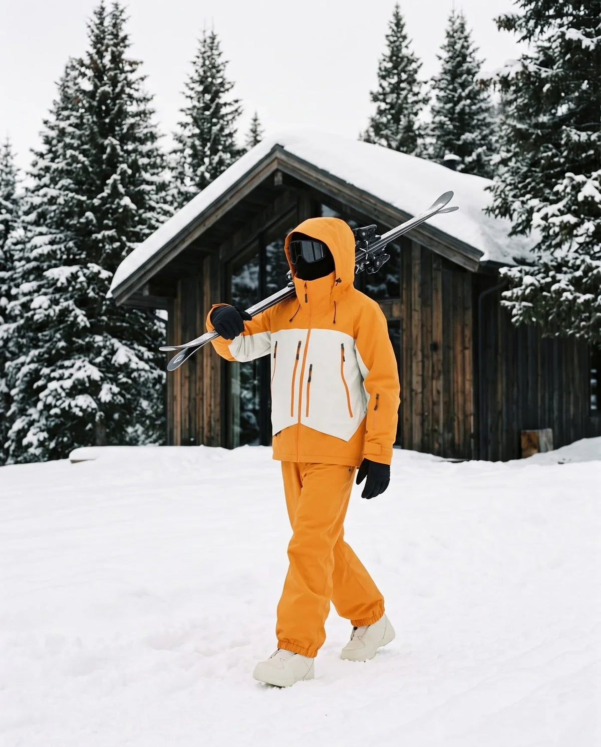 Combinaison de ski orange et blanc portée devant un chalet